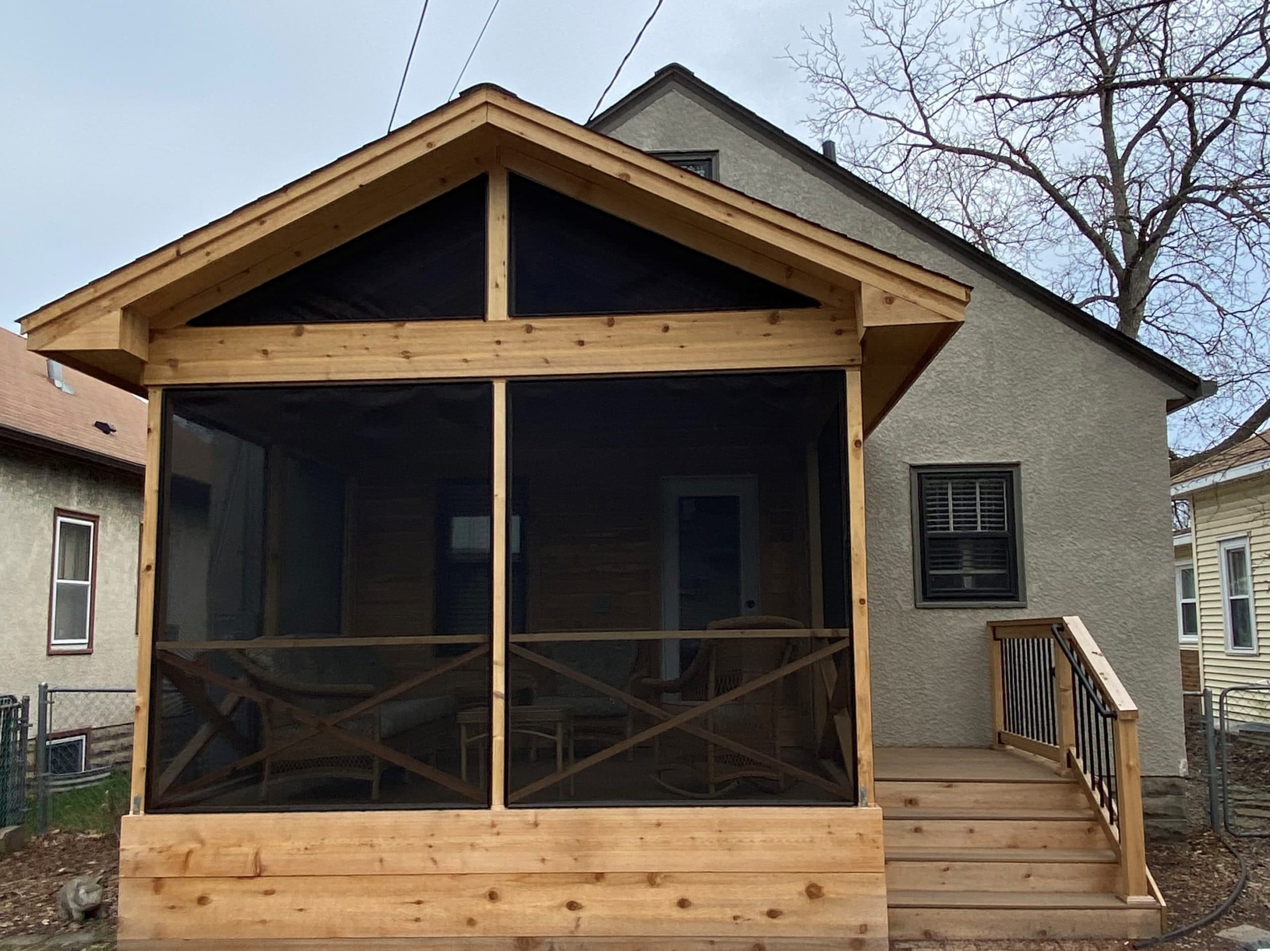 Wooden screened in porch with a short staircase descending to a ground patio